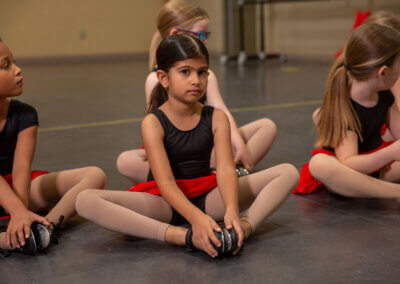 Graceful young girls dressed in ballet outfits, sitting on the floor, eagerly awaiting their turn to dance.
