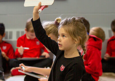A young girl proudly displays a piece of paper, her eyes shining with excitement and anticipation.